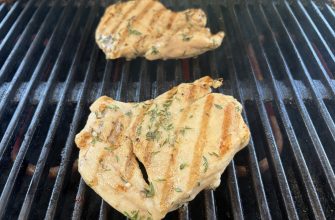 Herb-seasoned chicken grilling on a barbecue grill with visible char marks on the ribs.