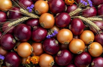 Pile of red and orange onions with wheat stalks and small purple flowers for a harvest scene.