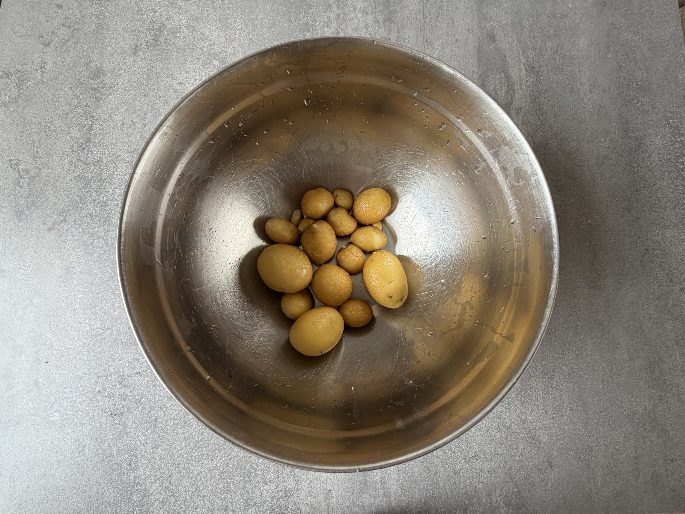 Metal bowl holding a handful of small yellow potatoes on a gray countertop.