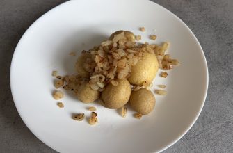 White plate topped with golden fried potato balls and sautéed onions, close-up.